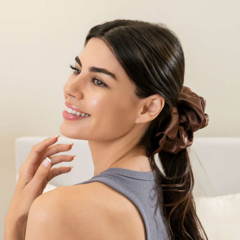 Brown silk scrunchie securing thick hair in a low ponytail for a stylish look with gentle, no-pull hold