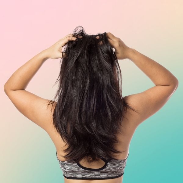 Woman with long dark hair scratching her itchy scalp with both hands, a common complaint with itchy scalp and hair loss
